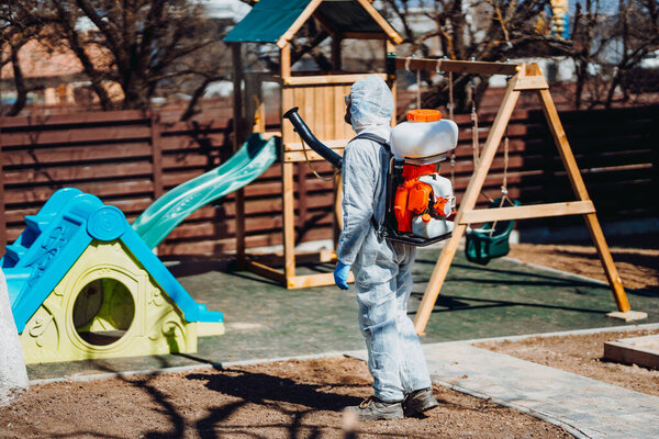 Белый мужчина в защитном защитном костюме распыляет дезинфицирующие средства и химикаты во время пандемии коронавируса
