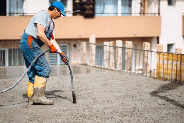 İnşaat alanında çimento dökerken beton vibratör kullanan beyaz işçi.
