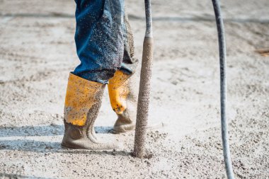 İnşaat işçisi çimento tabakasını titretiyor. Beton vibratör kullanan işçiler