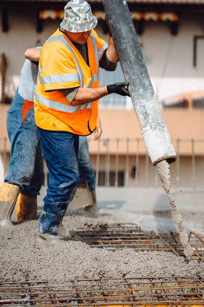 industrial workers pouring cement with manual pump tube