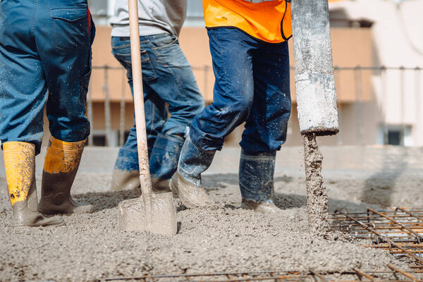 Caucasian workers pouring concrete on slab floor