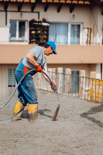 Caucasian construction worker using a concrete vibrator at the construction site during cement pouring in summer