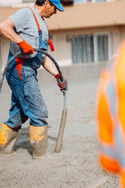 Caucasian construction worker using a concrete vibrator at the construction site during cement pouring