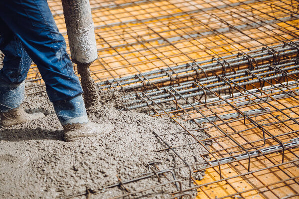 construction worker pouring cement or concrete with pump tube. Reinforced steel bars and rods