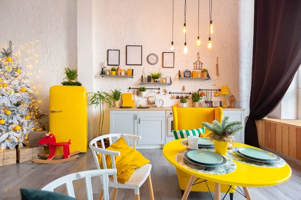 Trendy fashion luxury interior design in Scandinavian style of kitchen area in studio apartment with bright yellow furniture and decorated with new year tree.
