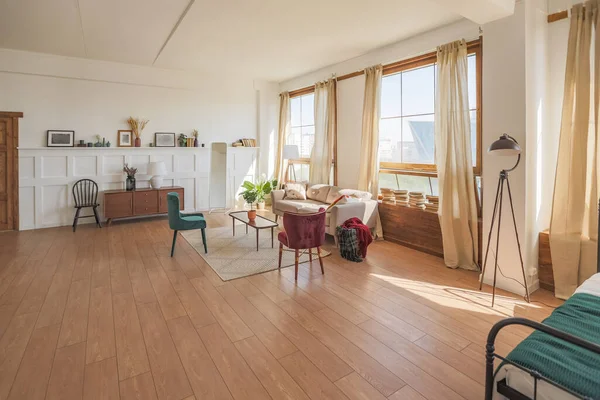Vintage studio apartment interior in light colors in old style, large windows with living room area and bedroom area, direct sunlight inside