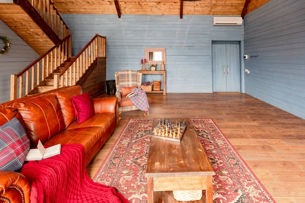 Interior of a country house in a wooden design, spacious living room with kitchen area and large windows, bedroom on the second floor