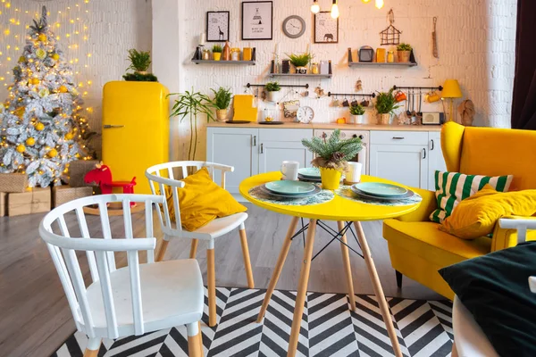 Trendy fashion luxury interior design in Scandinavian style of kitchen area in studio apartment with bright yellow furniture and decorated with new year tree.
