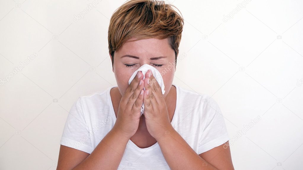 Short haired woman blowing her nose on the white background.