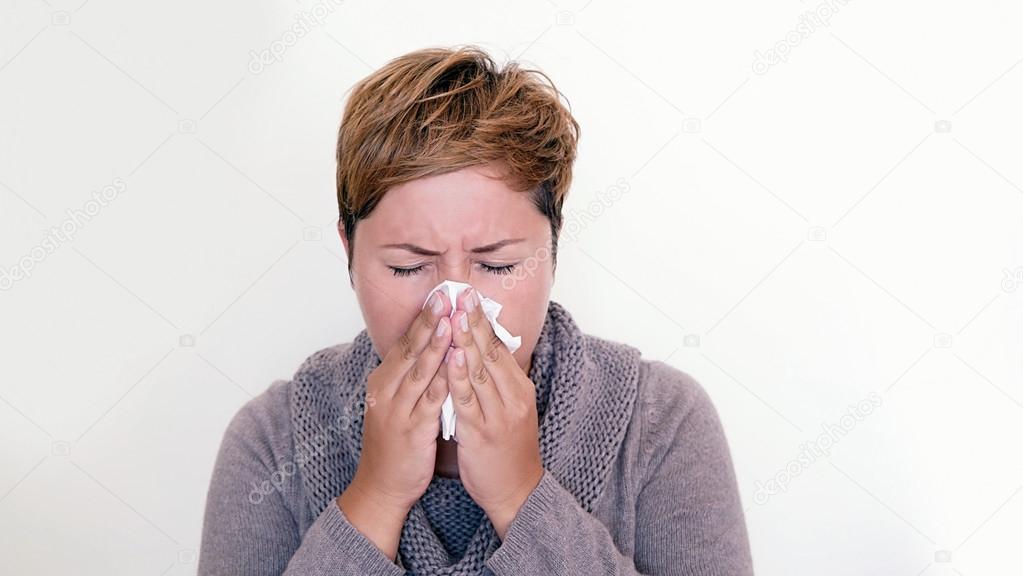 Short haired woman wearing a sweater blowing her nose
