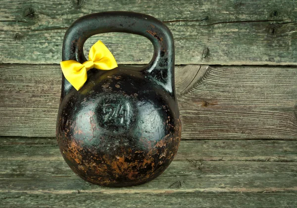 Vintage oude kettlebell met een gele gebonden strik op een houten achtergrond. — Stockfoto