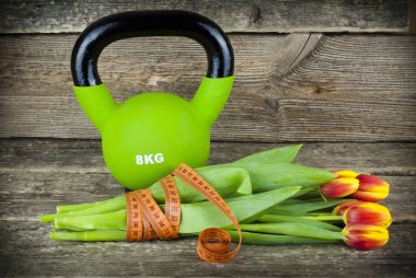 Kettlebells yeşil ve bir ölçüm bandı buket Lale çiçek ahşap arka plan üzerinde ile bağlı.
