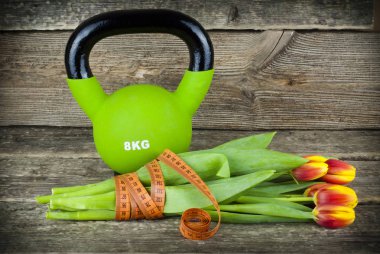Green kettlebells and tied with a measuring tape bouquet of tulips flowers on a wooden background. clipart