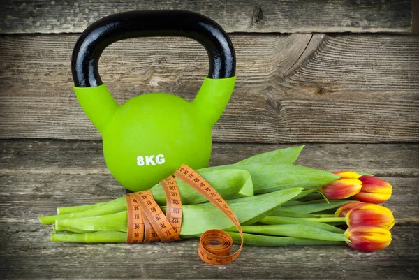 Kettlebells yeşil ve bir ölçüm bandı buket Lale çiçek ahşap arka plan üzerinde ile bağlı.