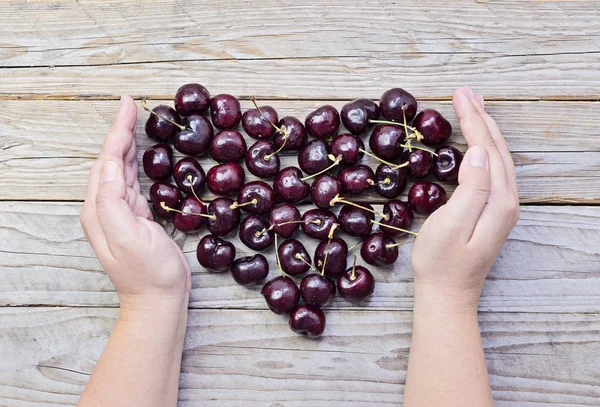 Corazón de cerezas frescas y maduras en manos femeninas con copas — Foto de Stock