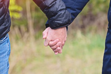 Two men holding hands in jackets outdoor, closeup view