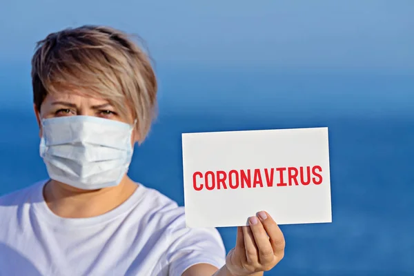Kvinna i kirurgisk mask håller blankt med text coronavirus 2019 — Stockfoto