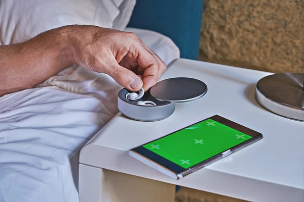 Man takes one of noise-masking sleepbuds from holder on table