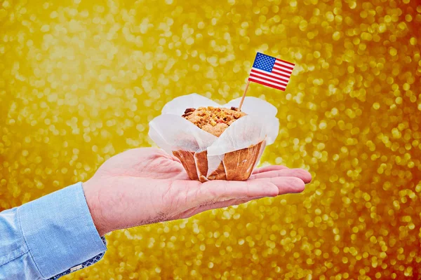 Cupcake with American flag on male palm against golden glitter background — Stock Photo, Image