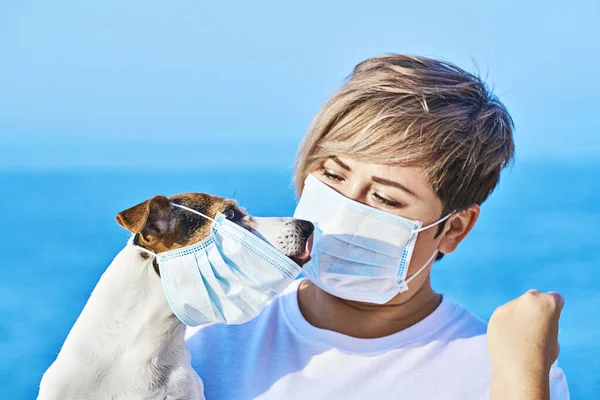 Woman in protective face mask looking at dog wearing medical mask Stockfoto