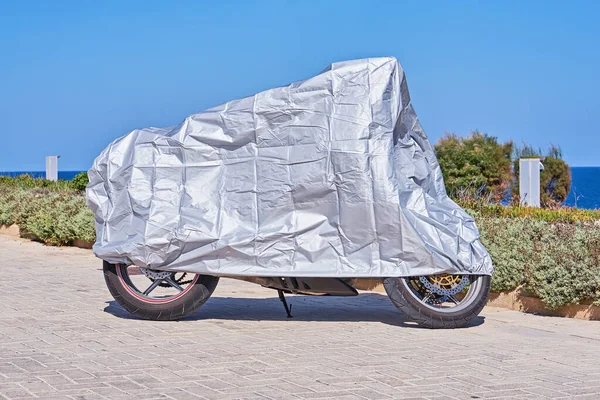Gümüş yansıtıcı yüzeyli motosiklet için su geçirmez kaplama. Motosiklet, açık havada park edilmiş kumaş kalkanla kaplı.