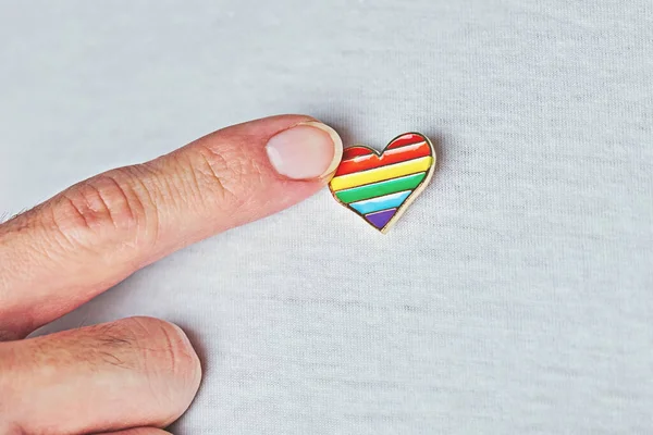 LGBT Pin badge in heart-shaped on white t-shirt and male forefinger. Concept of celebration of LGBTQ Pride flag day and people rights