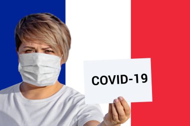 Yüz maskeli kadın, Fransız bayrağına karşı Covid-19 yazılı kağıt tutuyor. Çin Coronavirüs Covid-19 romanı Coronavirus pnömoni virüsünün tüm dünyaya yayılması konsepti