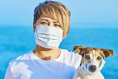 Koruyucu maskeli bir kadın ve tıbbi maske takan bir köpek. Çin Coronavirüs Hastalığı COVID-19 evcil hayvanlar için tehlikelidir.