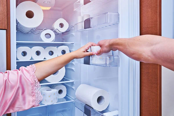 Female and male hand grab hold of last toilet paper roll on fridge door. Concept of over-buying toilet paper during coronavirus