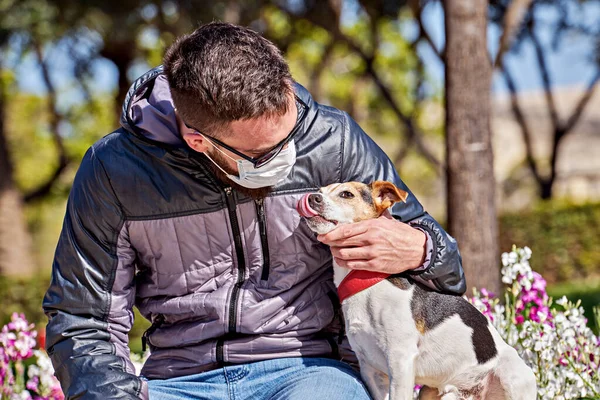 Coronavirus sırasında maskeli bir adam köpeği öpüyor. Covid-19 salgını sırasında kısa yürüyüşler. covid-19 sırasında evcil hayvanla temastan kaçının
