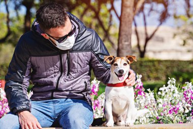 Coronavirus sırasında yüz maskesi takan bir adam köpeğe bakıyor. Covid-19 salgını sırasında kısa yürüyüşler. covid-19 sırasında evcil hayvanla temastan kaçının