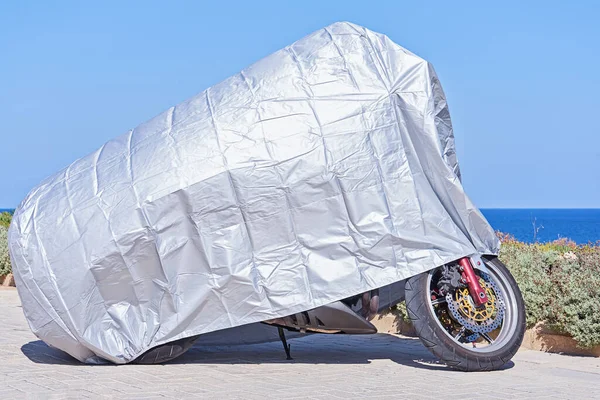 Waterproof cover for motorcycle with silver reflective protective surface. Motorbike covered with fabric shield parked at outdoor