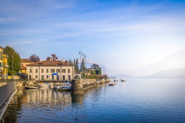 Pacifying morning landscape with snowy peaks of Alps and calm water surface of Lake Como on shores of authentic town of Dongo in Italy clipart