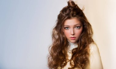 Açık sarı ve mavi arka planda güzel bir kadının portresi. Uzun, gür saçlar, şık bir çörek, saç stili. Temiz, sağlıklı cilt.