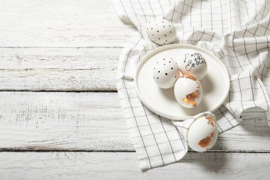 Beyaz ahşap arka planda bir tabakta güzel paskalya yumurtaları, yazı için yer, üst manzara.