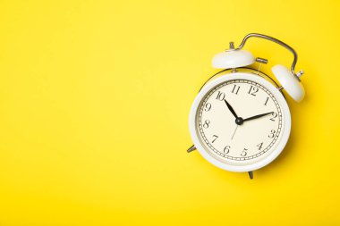 Sarı arka planda beyaz alarmlı saat. Üst görünüm, metin için yer.