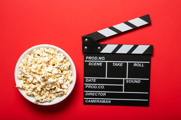 Plate with popcorn and movie clapper board on a red background