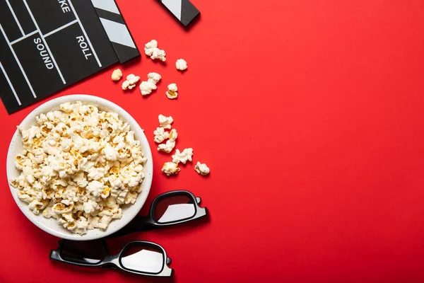 Plate with popcorn and movie clapper on a red background. Place for text