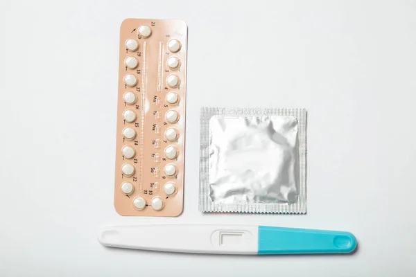 Female birth control pills, pregnancy test and condom on a white background