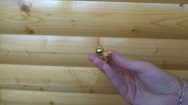 New gold fidget Orbiter,spinning in the hand of a young man on wooden background — Stock Video