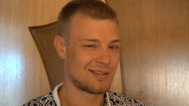 Close-up do jovem sorridente olhando para a câmera isolada no fundo branco. Retrato de um tipo com barba que muda as expressões faciais. Orgulhoso e satisfeito homem com t-shirt olhando para a câmera — Vídeo de Stock