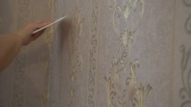 Duvardaki bir spatula sıkma ile duvar kağıdı yumuşatmak için çalışan el duvar kağıdı yapıştırma işlemi