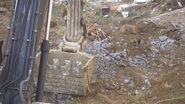 Graafmachine verplettert een emmer van de rotsen naast een vuile grond — Stockvideo