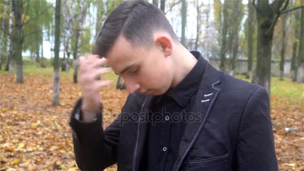 Όμορφος νεαρός άνδρας στο σμόκιν ισιώνει τα μαλλιά τους το φθινόπωρο πάρκο — Αρχείο Βίντεο