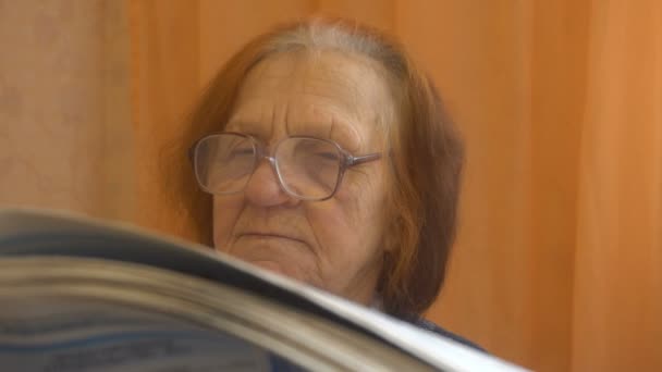 Old woman in glasses reads the newspaper carefully — Stock Video