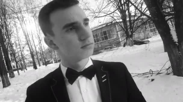 Jeune homme posant en smoking en hiver contre la neige blanche, tourné dans un style rétro — Video