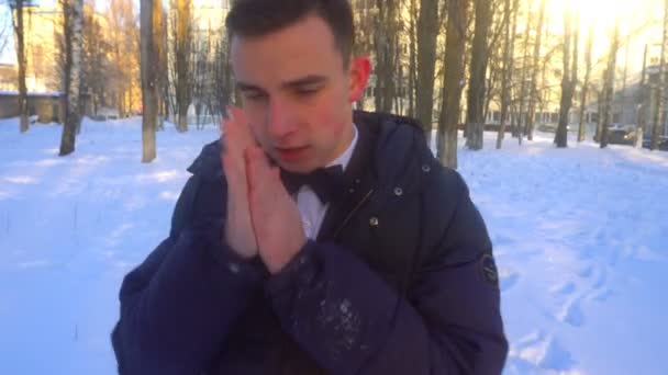 Молодой человек пытается согреться зимой, стоя в снегу — стоковое видео
