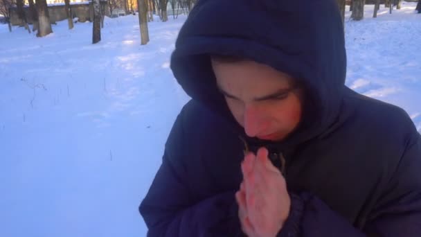 Um jovem tenta manter-se quente no inverno, de pé na neve — Vídeo de Stock