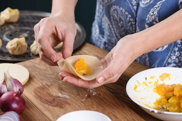 Cooking technique. Woman hands making Asian steam dumplings with pumpkin