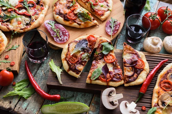 Pizza party flatlay. Set of homemade rustic pizzas served with raw vegetables, mushrooms and red wine on shabby blue background